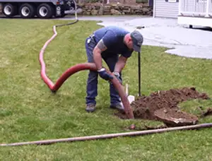 Septic pumping technician servicing a residential septic tank with a vacuum hose in Plymouth, MA