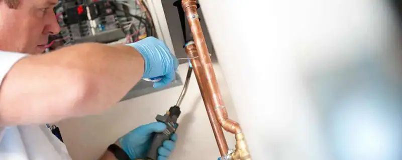 Water heater repair technician testing copper pipe connections and controls in Plymouth, MA